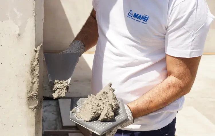 Mapei Austria Marke Bauchemie.at Onlineshop - Mann trägt mit Spachtel Mapei Produkt auf eine Wand auf